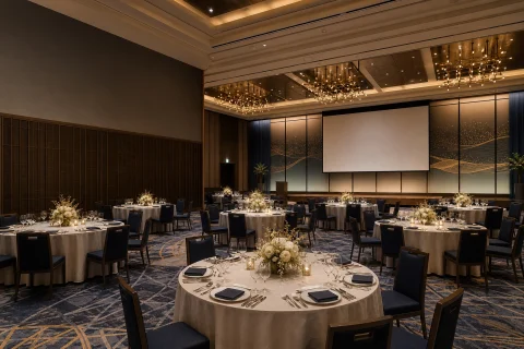 名古屋のホテルで企業の忘年会・新年会を開くイメージ。円卓、料理台、受付、ステージ、無地スクリーンがある上質な宴会場